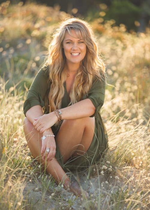 Photo of author Emma Mildon sitting in a field of grass and smiling at the camera